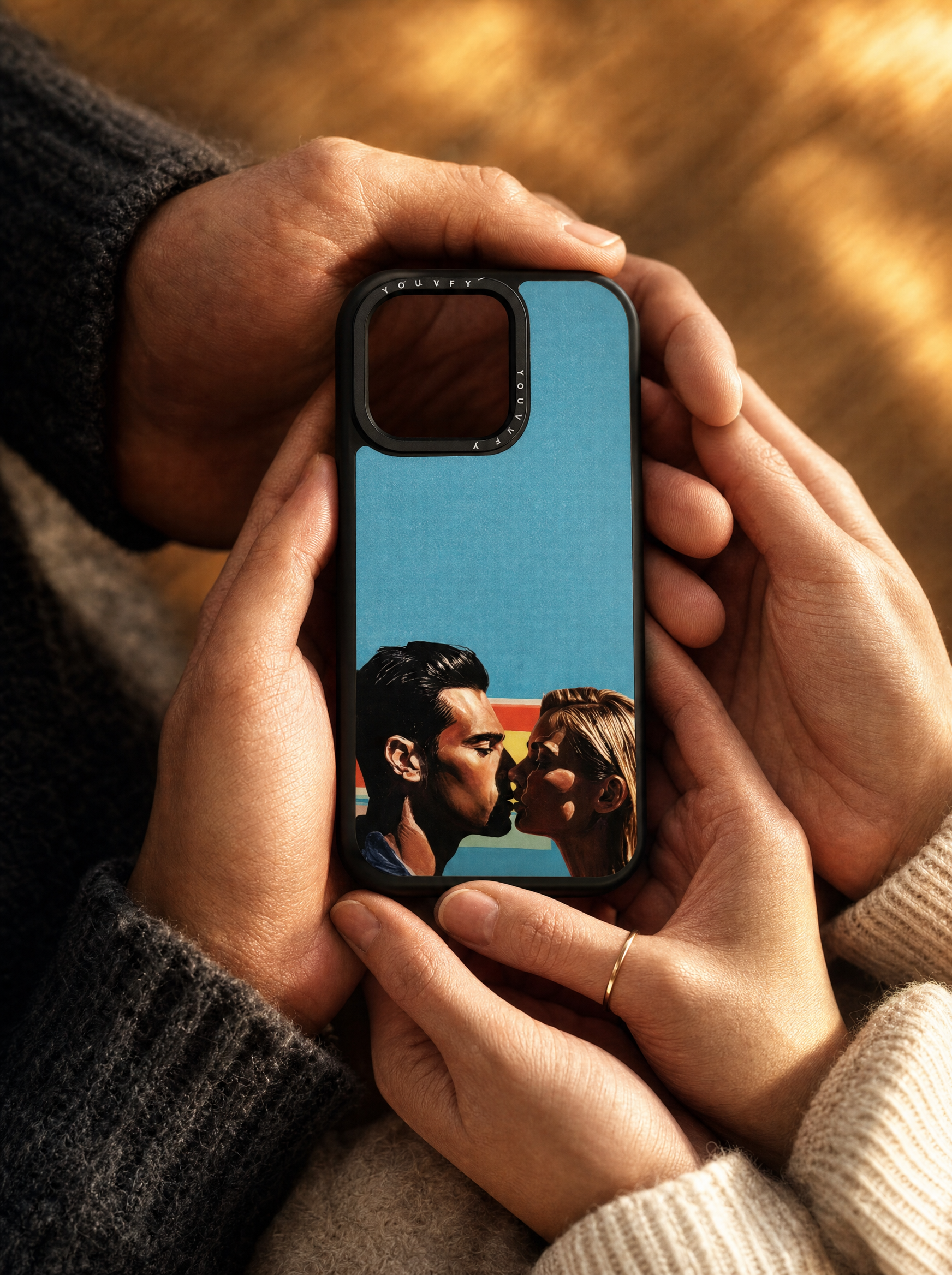 Couple's hands tenderly holding a Youvfy iPhone case with an illustrated couple kissing portrait, golden hour