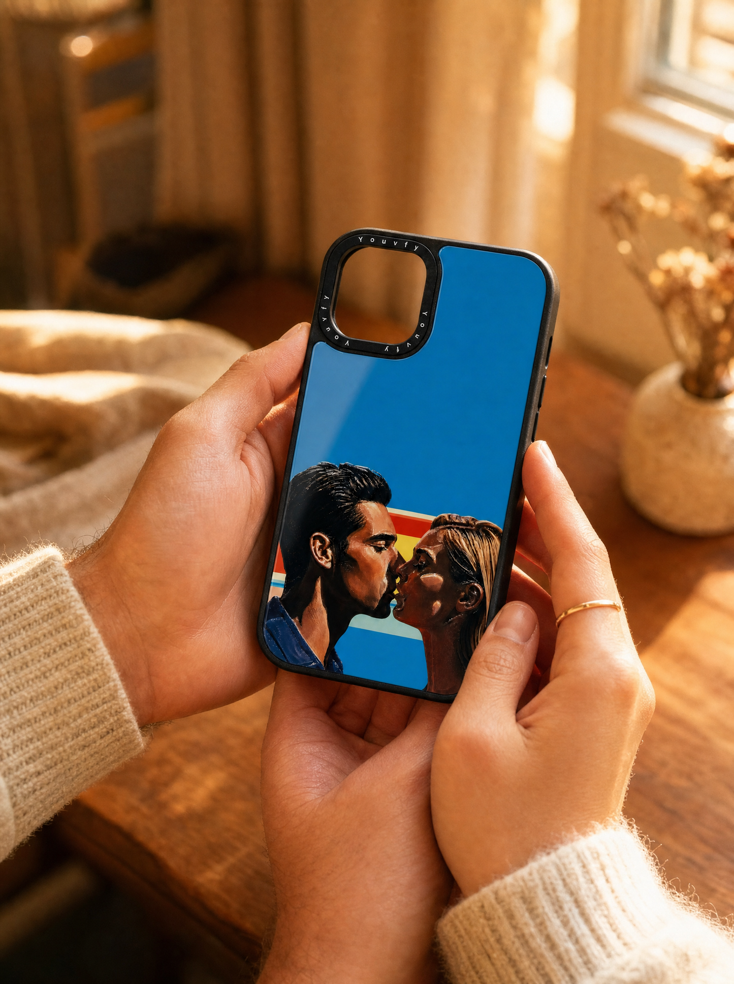 Couple's hands tenderly holding a Youvfy flat-printed iPhone case with an illustrated couple portrait, golden hour