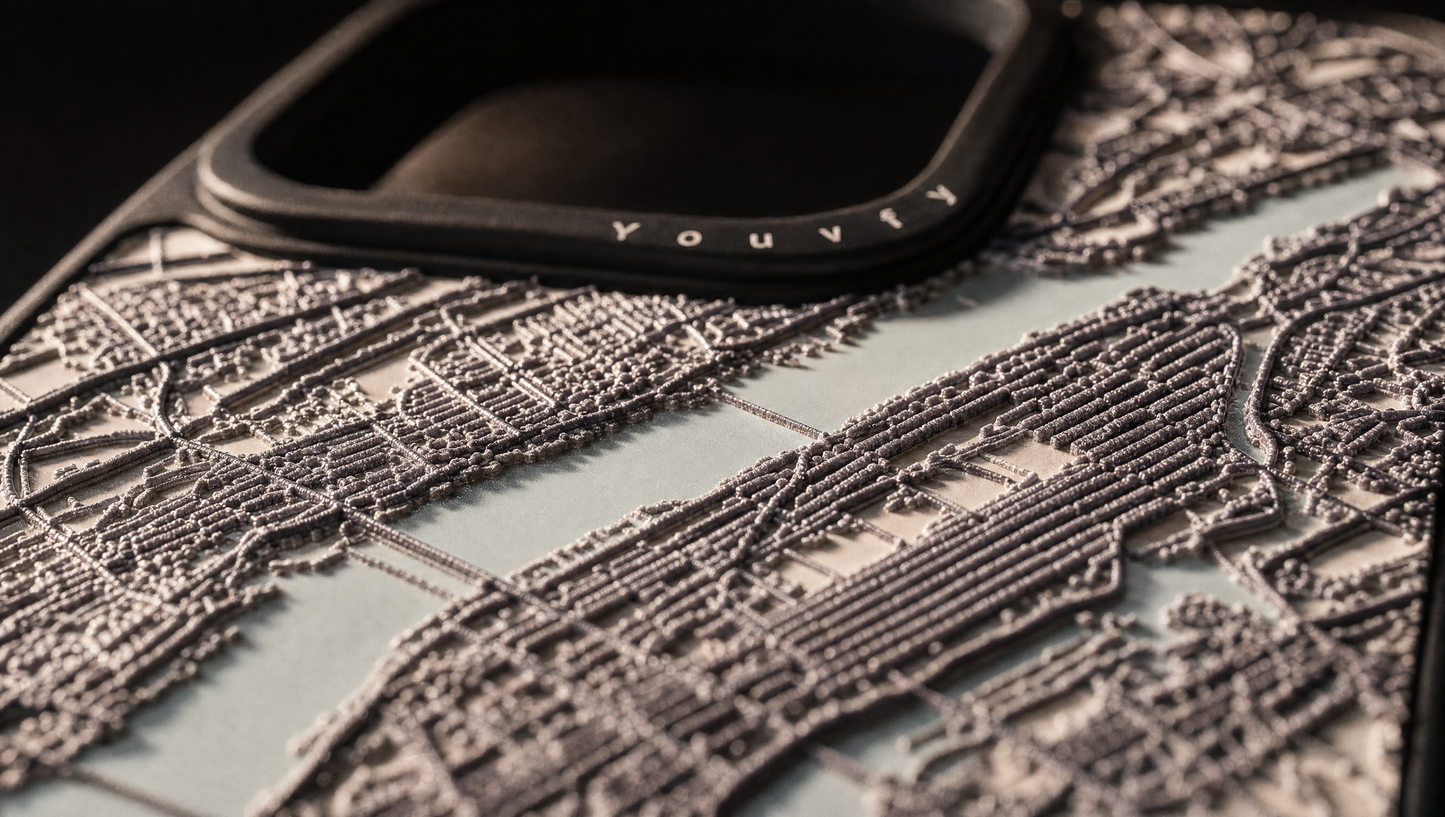 Extreme low side-angle macro of a Youvfy NY map case showing the raised 2.5D streets standing in profile against raking light