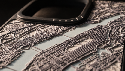 Extreme low side-angle macro of a Youvfy NY map case showing the raised 2.5D streets standing in profile against raking light